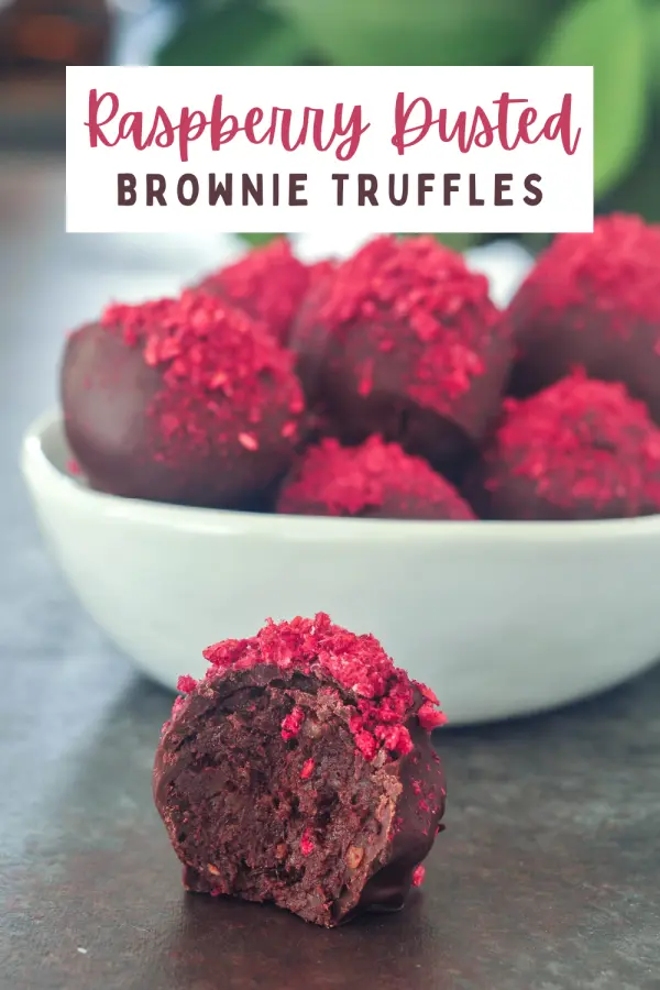 dark chocolate truffles with freeze dried raspberry dust in a white bowl, one out of the bowl and sliced in half to show the brownie filling.