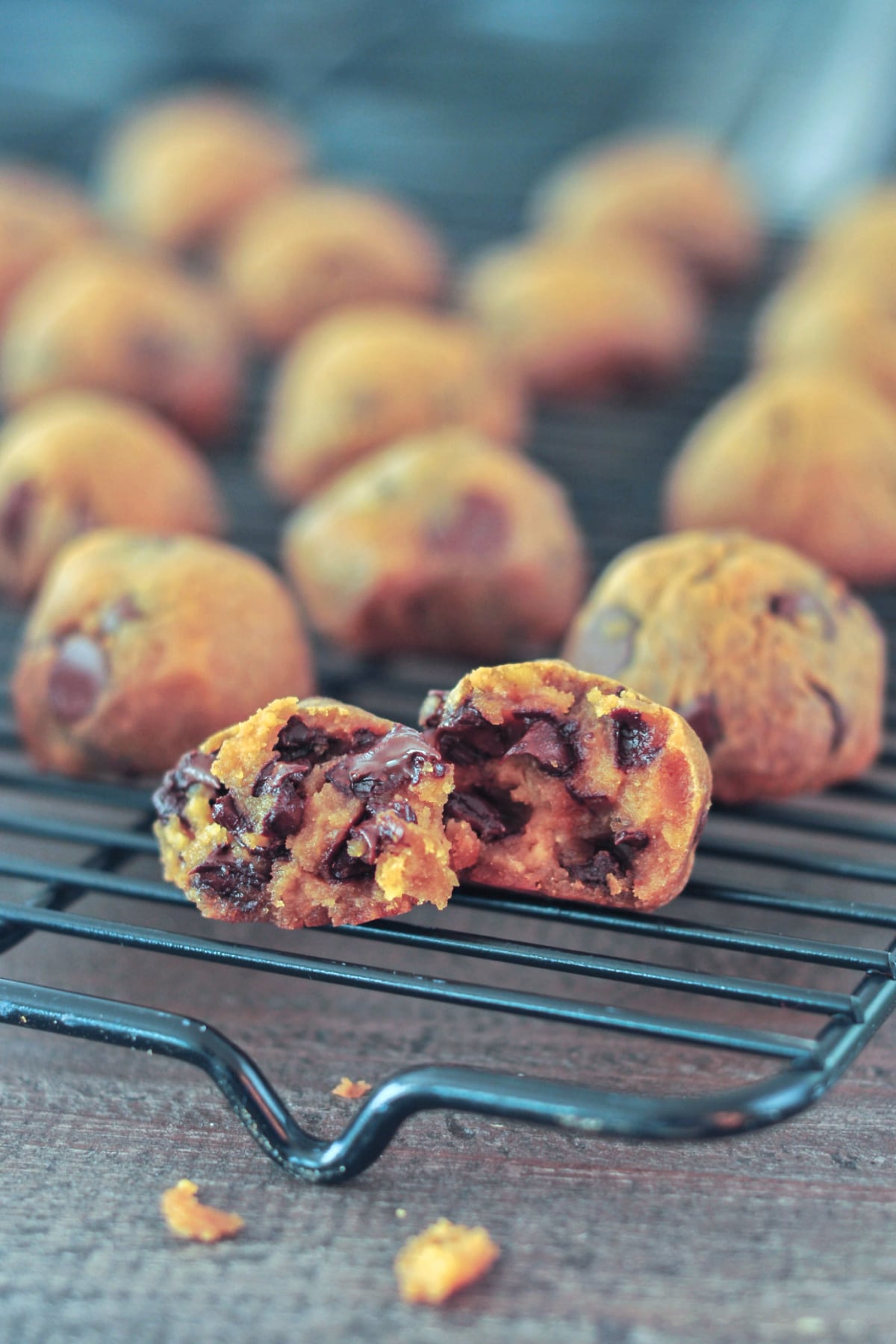 chickpea cookie balls on a cooling rack. one cookie is split in half to show melty chocolate chips inside.