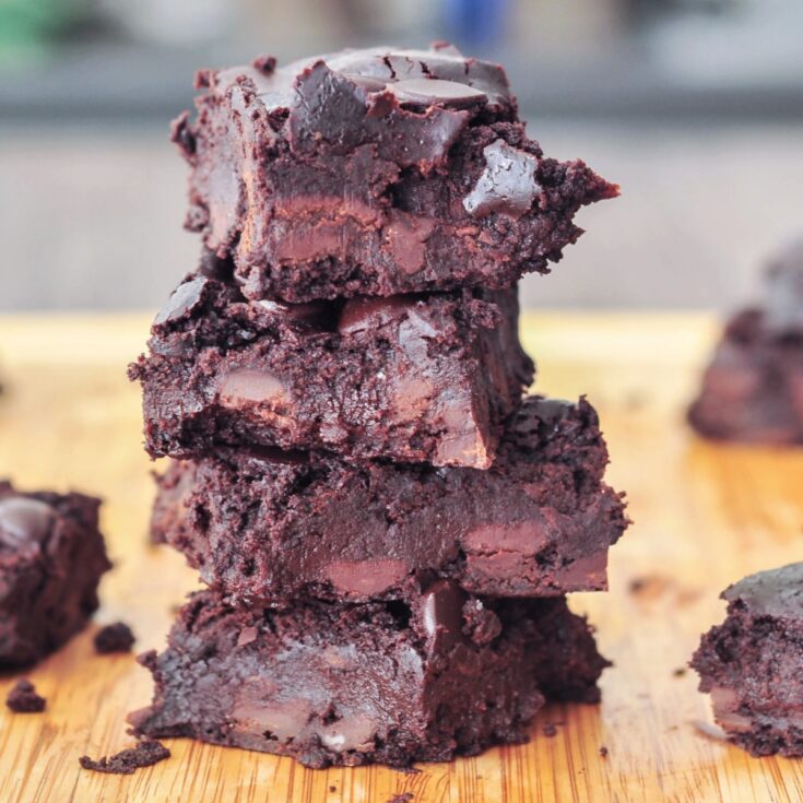 a stack of four chocolate black bean brownies on a light tan bamboo cutting board