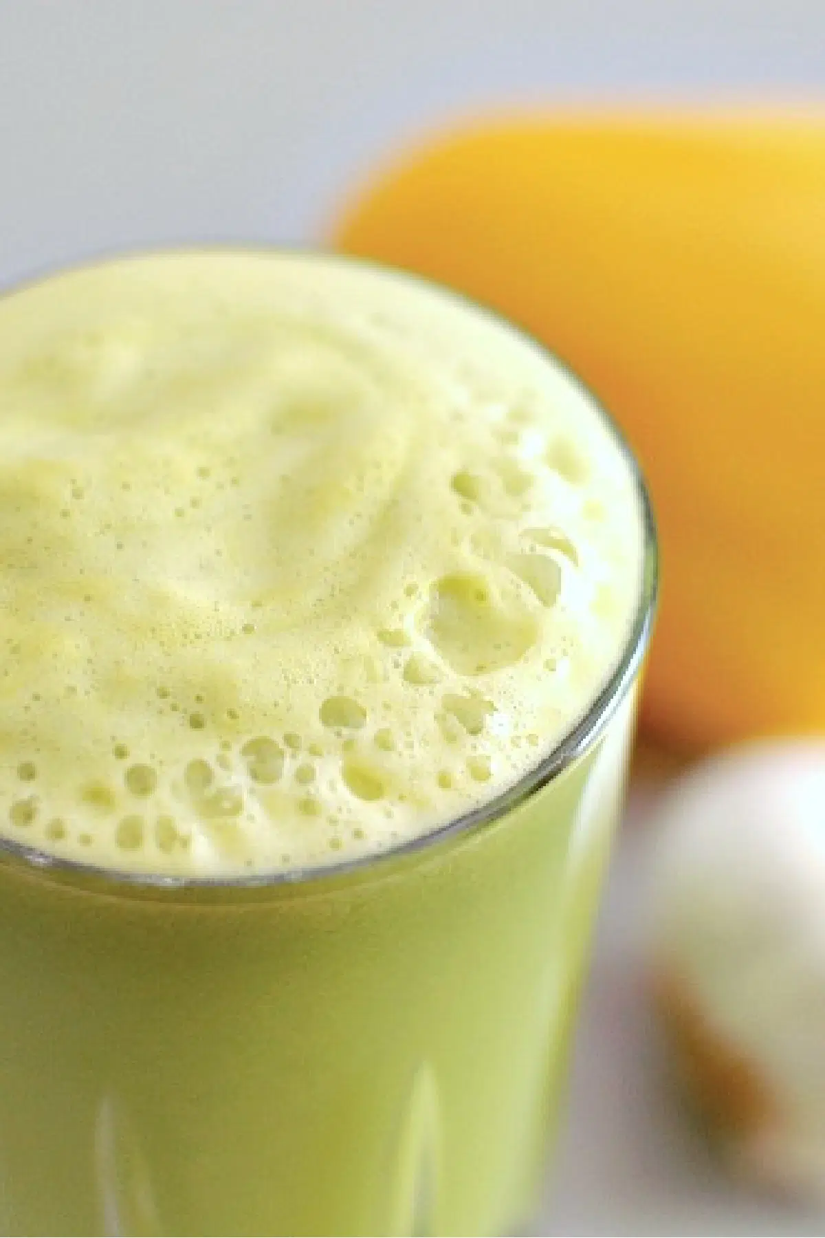 overhead view of a glass of garlic apple juice. bright green juice showing through the glass, with a light green foamy top. yellow bell pepper and whole garlic bulb in background.