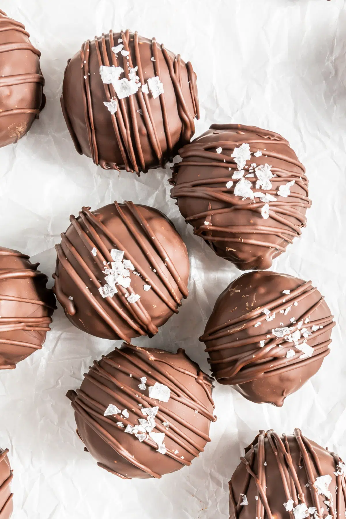 overhead view of chocolate covered peanut butter crunch balls with flaked sea salt, sitting on white parchment paper