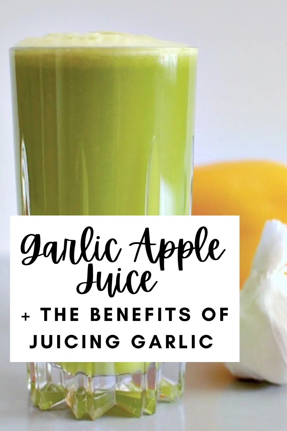 side view of bright green garlic apple juice in a tall cut crystal glass. juice has light green foam on top, and there is a yellow bell pepper and a white bulb of garlic sitting beside the glass of juice.