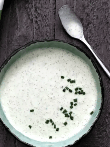 overhead view of vegan ranch dressing in a bowl, topped with chopped chives. green and white napkin and small spoon next to bowl.