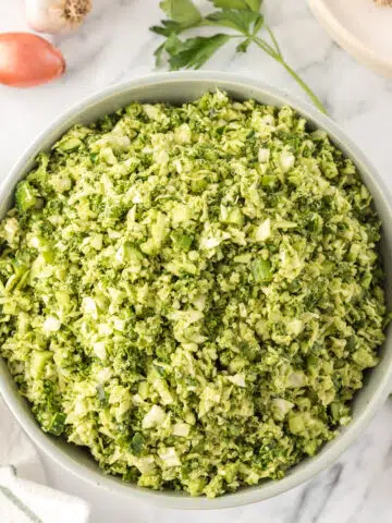 overhead view of green goddess chopped salad: a white bowl filled with finely chopped cabbage, cucumbers, green onions, kale, and cooked quinoa with a bright herby green goddess dressing.