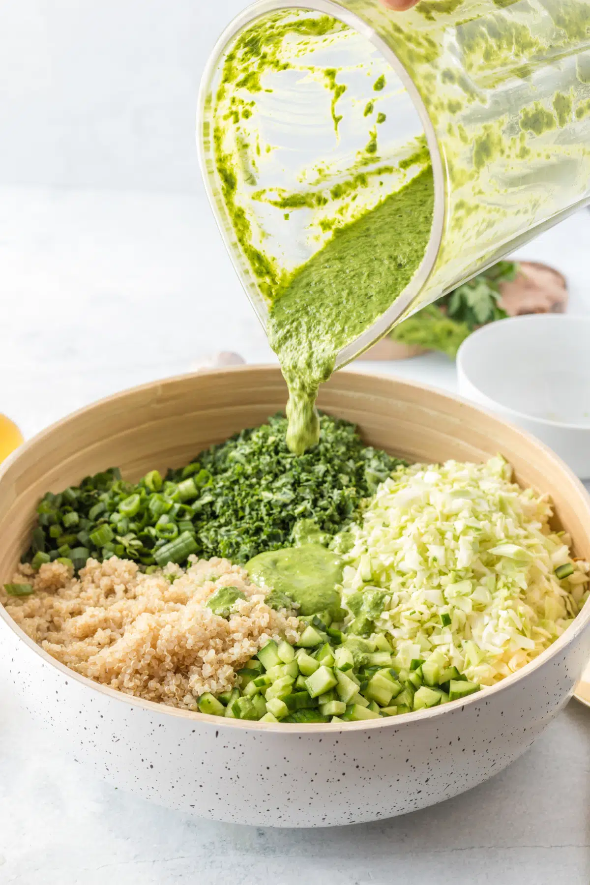 green goddess dressing being poured over chopped salad in a bowl, before mixing