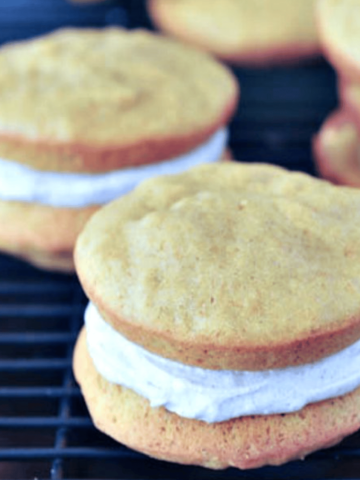 Pumpkin whoopie pies with ginger cream frosting on a cooling rack against a dark background