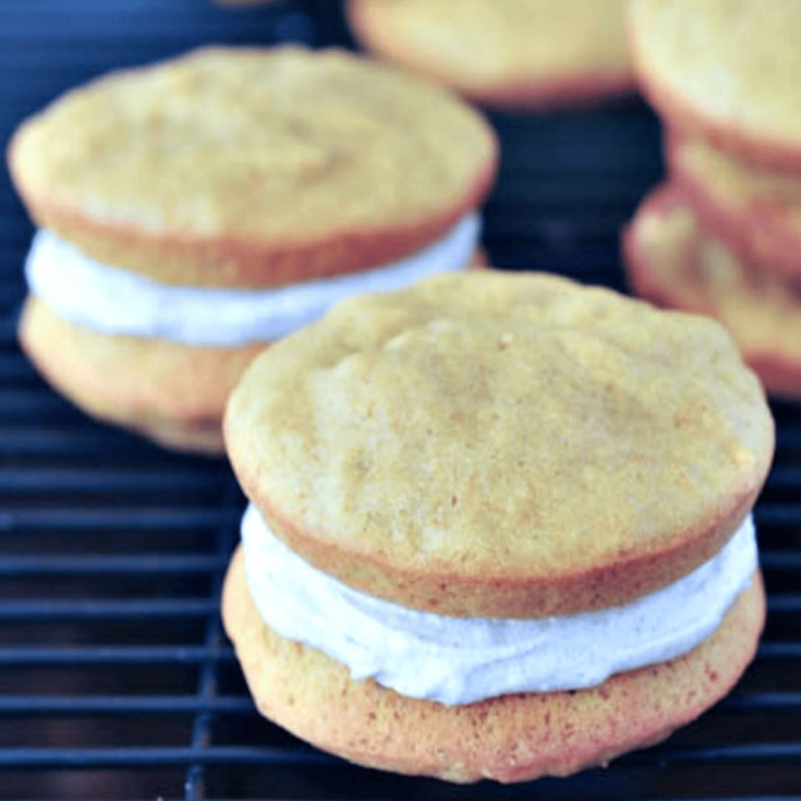 Pumpkin whoopie pies with ginger cream frosting on a cooling rack against a dark background