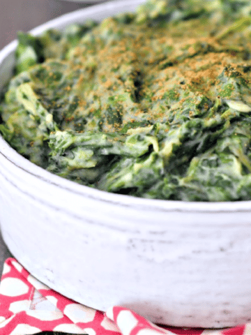 vegan creamed spinach in a rustic white round serving dish, red napkin underneath