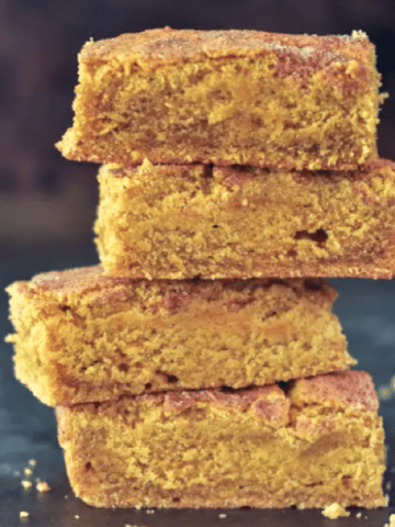 side view of a stack of four vegan pumpkin blondie squares against a dark background.