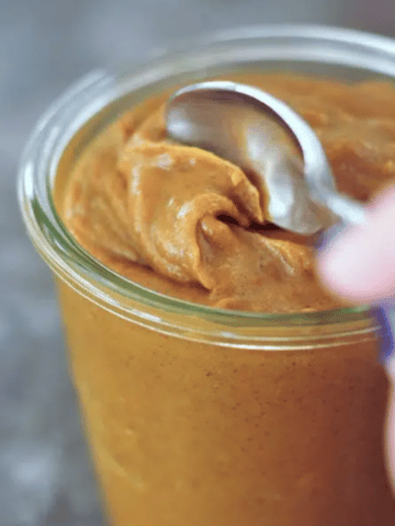 a spoon going into a glass jar of pumpkin caramel