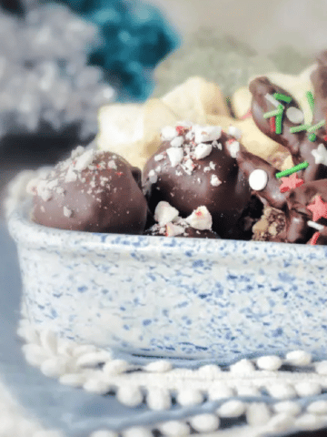 a white ceramic dish with blue splatter paint holds holiday cookies and candies, like chocolate covered pretzels shaped as reindeer, peppermint oreo truffles, shortbread star shaped cookies
