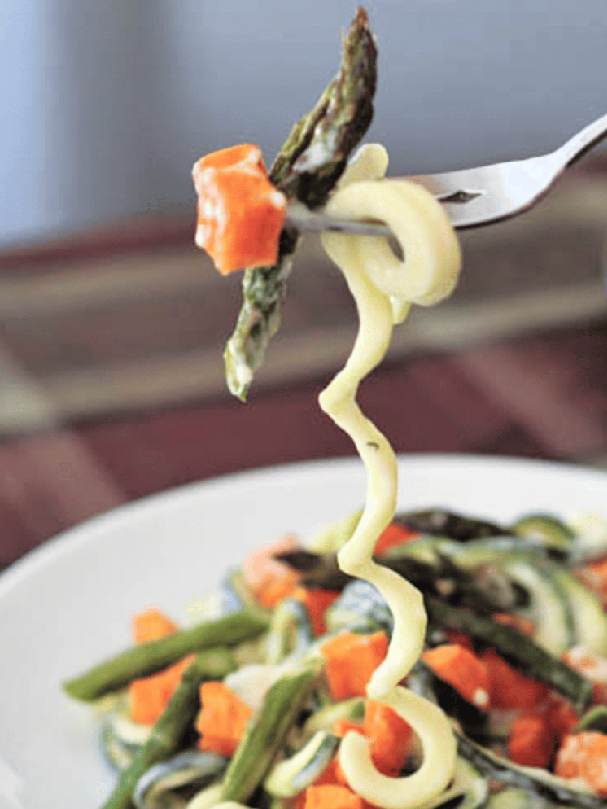 one bite of roasted sweet potato asparagus pasta on a fork, with one long curly zucchini noodle hanging down off fork