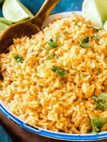 serving bowl of Spanish Rice with lime wedges and wooden spoon, garnished with cilantro
