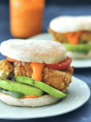 Air fried tofu sandwich with avocado, tomato, spinach in an English muffin, served on a green dish