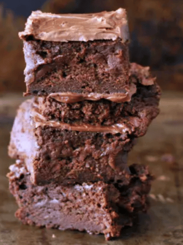 a stack of four frosted vegan brownies against a dark marbled background