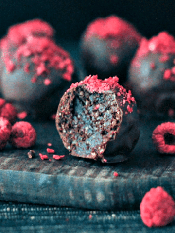 chocolate truffles with freeze dried raspberry dust on a dark wood board, one truffle sliced in half to show the brownie filling.