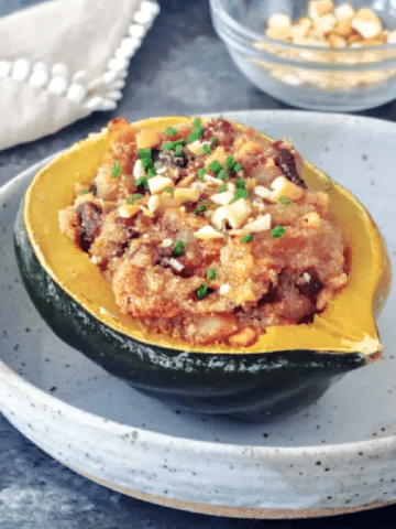 stuffed acorn squash: an amaranth grain mixture stuffed into a half an acorn squash, served in a grey rustic shallow bowl, topped with cashews and chives