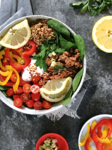 overhead view of a deconstructed stuffed pepper bowl (spinach and greens, vegan ground beef, cherry tomatoes, bell pepper slices, green onion and cilantro)