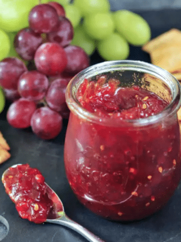 open glass jar of tomato refrigerator jam on a snack tray with crackers and grapes
