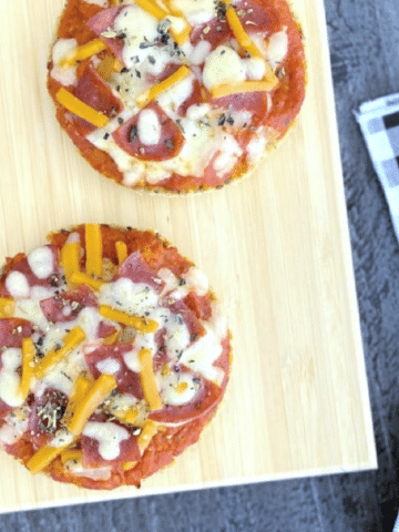 overhead view of two English Muffin Pizzas on a cutting board, with a black and white checkered cloth napkin on the side.