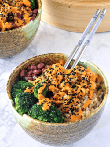 two kimchi bowls with beans, rice, broccoli, and red curry almond sauce, broccoli in bamboo steamer on the side
