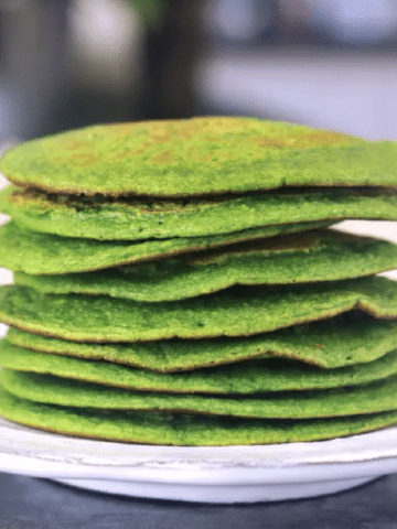 a stack of green spinach pancakes on a white rustic plate.