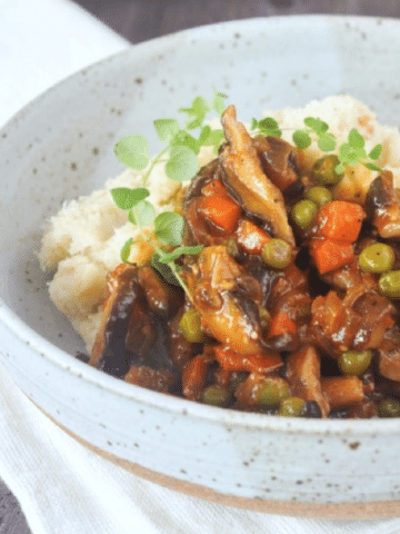 bowl of mushroom stew served over mashed cauliflower, sprig of fresh green thyme on top