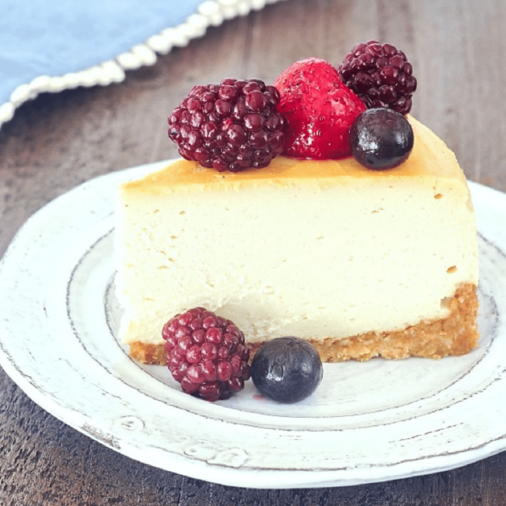 One slice of vegan cheesecake on a rustic white plate with fresh blackberries, blueberries and a strawberry.