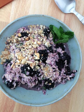 overhead view of a bowl of lavender colored overnight oats topped with berries, a mint leaf, and chopped cashews.