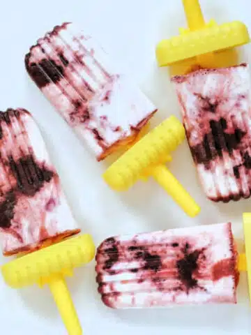 Cherry cheesecake popsicles with shortcake crumb on bright yellow handles on a white ceramic platter