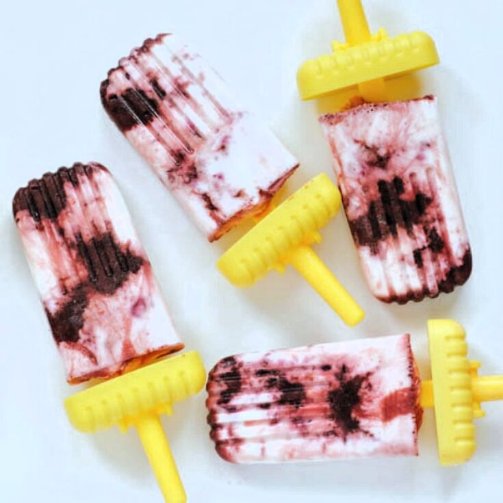 Cherry cheesecake popsicles with shortcake crumb on bright yellow handles on a white ceramic platter