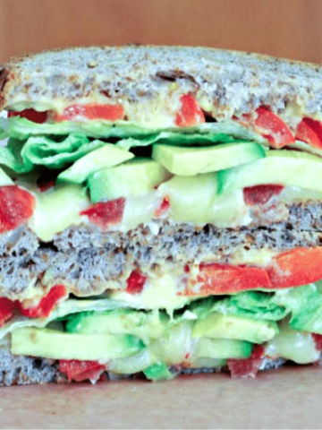 side view of a fresh vegetable grilled cheese sandwich with avocado, tomatoes, lettuce, one half stacked on top of other half.