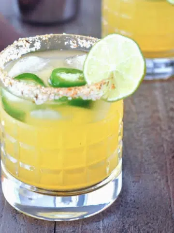 a jalapeno margarita in a rocks glass with a salted rim. orange and lime on the side.