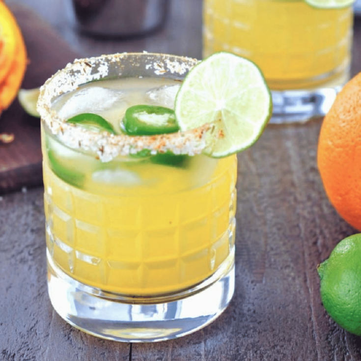 a jalapeno margarita in a rocks glass with a salted rim. orange and lime on the side.