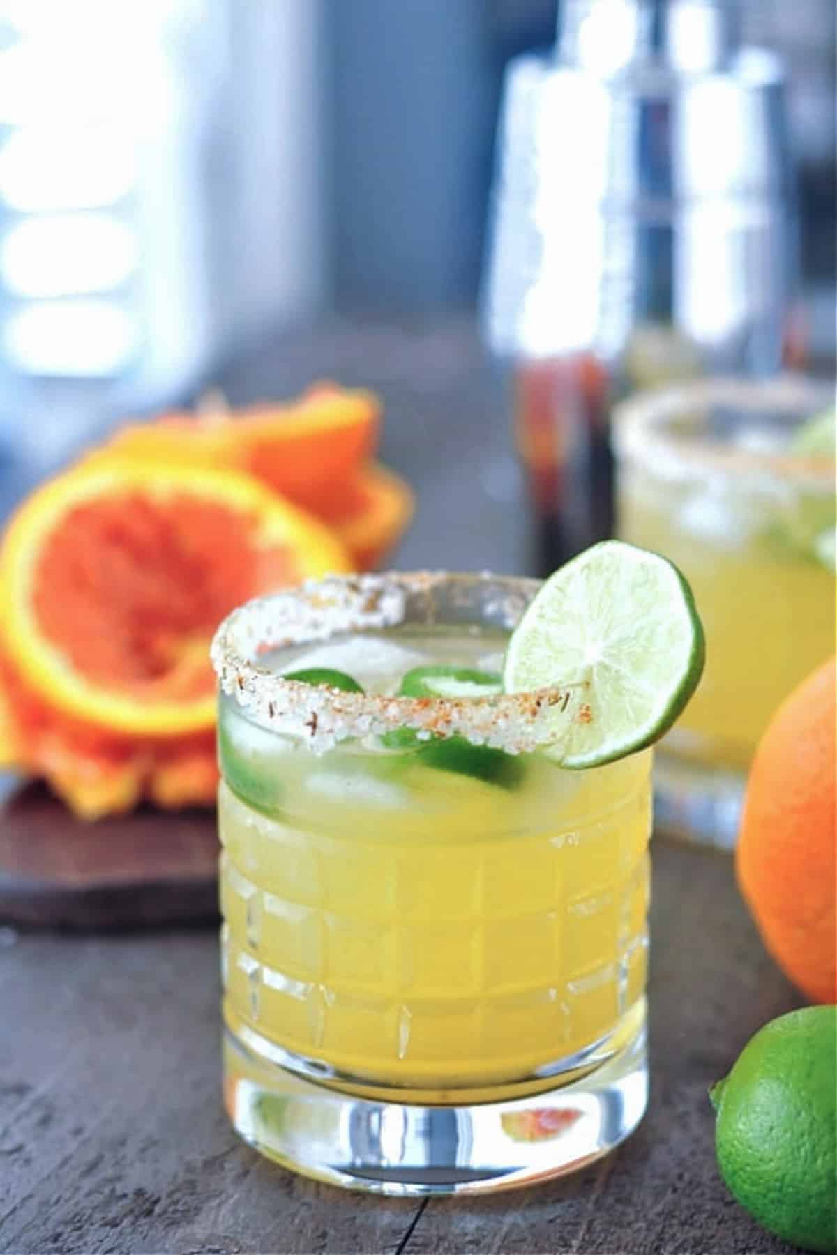 a jalapeno margarita in a rocks glass with a salted rim. orange and lime on the side.