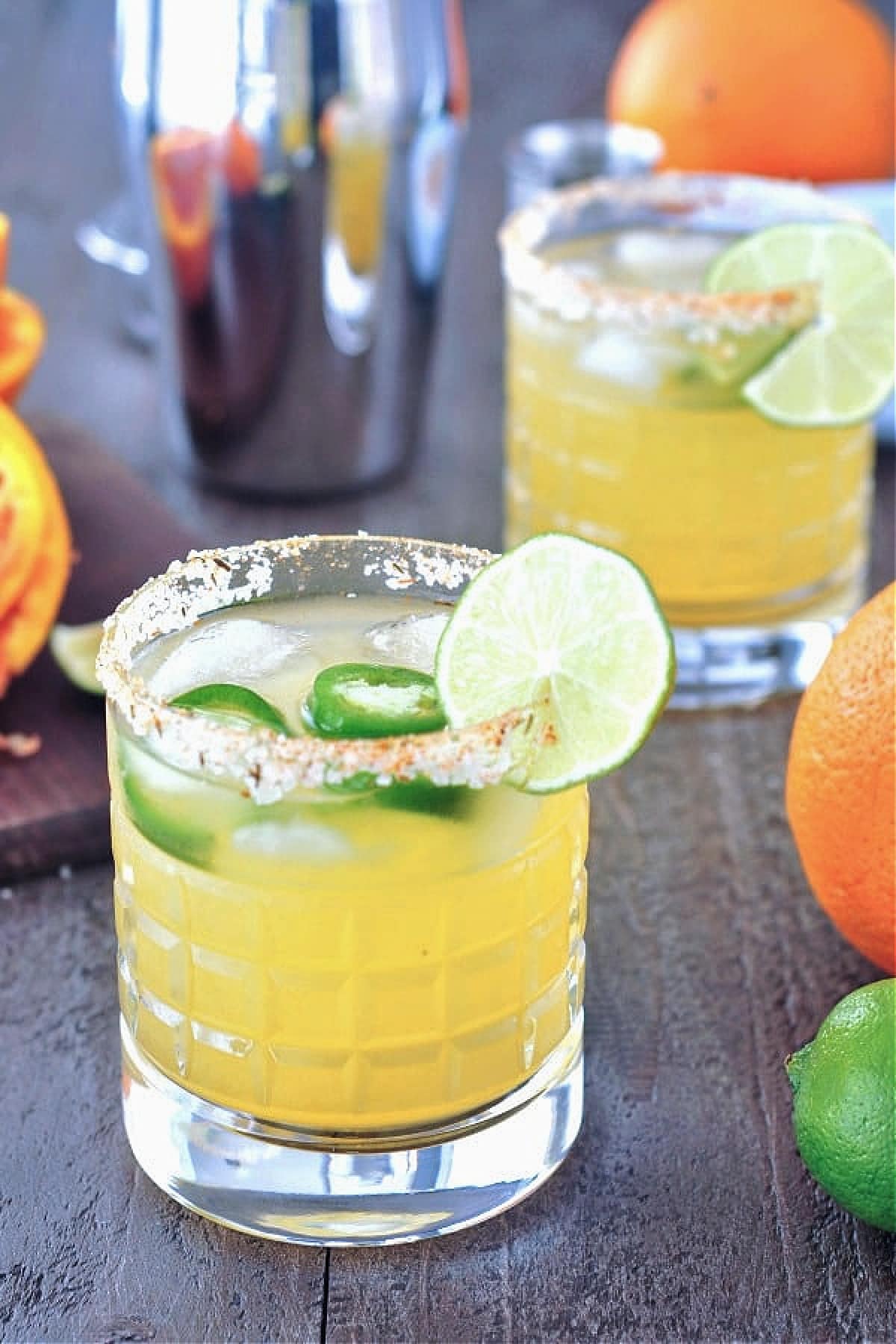 a jalapeno margarita in a rocks glass with a salted rim. orange and lime on the side.