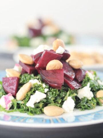 Roasted beet salad with vegan goat cheese, kale, and marcona almonds on a plate with a teal and gold Greek key design on the rim.