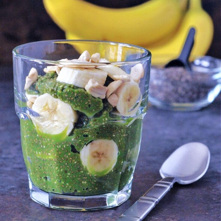 bright green pineapple chia pudding in a glass with banana slices. the green color comes from fresh spinach added for protein.