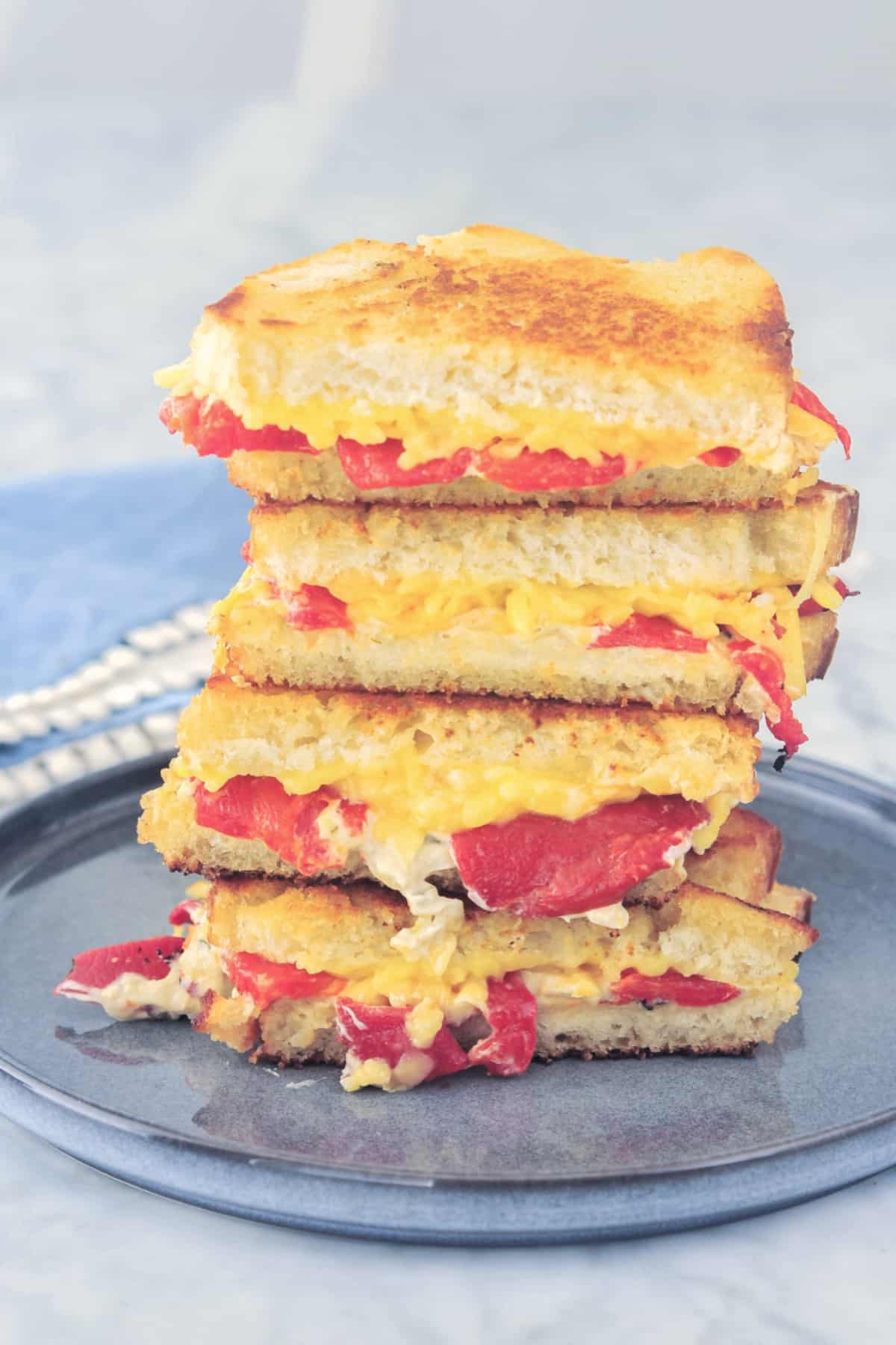 a stack of four sandwich halves of roasted red pepper grilled cheese on a dark grey plate. light blue napkin with white border in background.