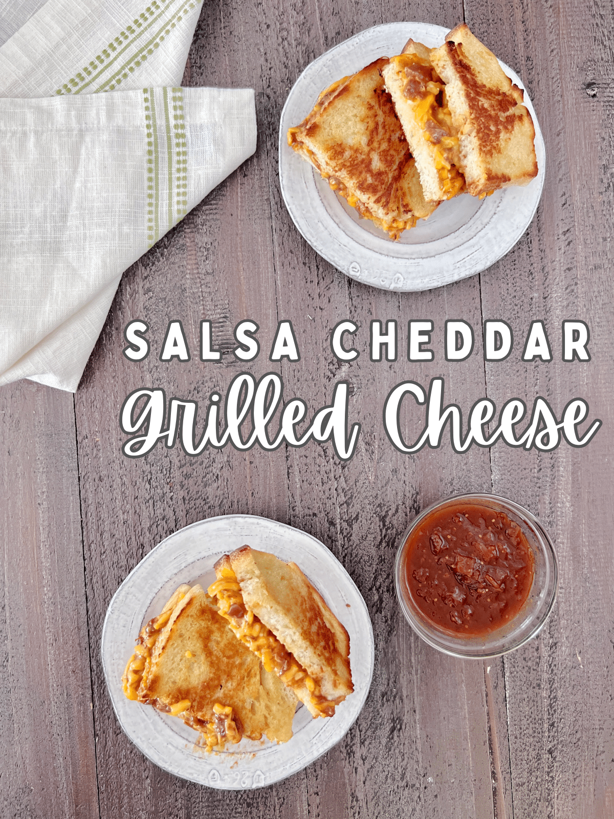 overhead view of two salsa cheddar grilled cheese sandwiches on rustic white plates next to a small glass bowl of extra salsa for dipping.