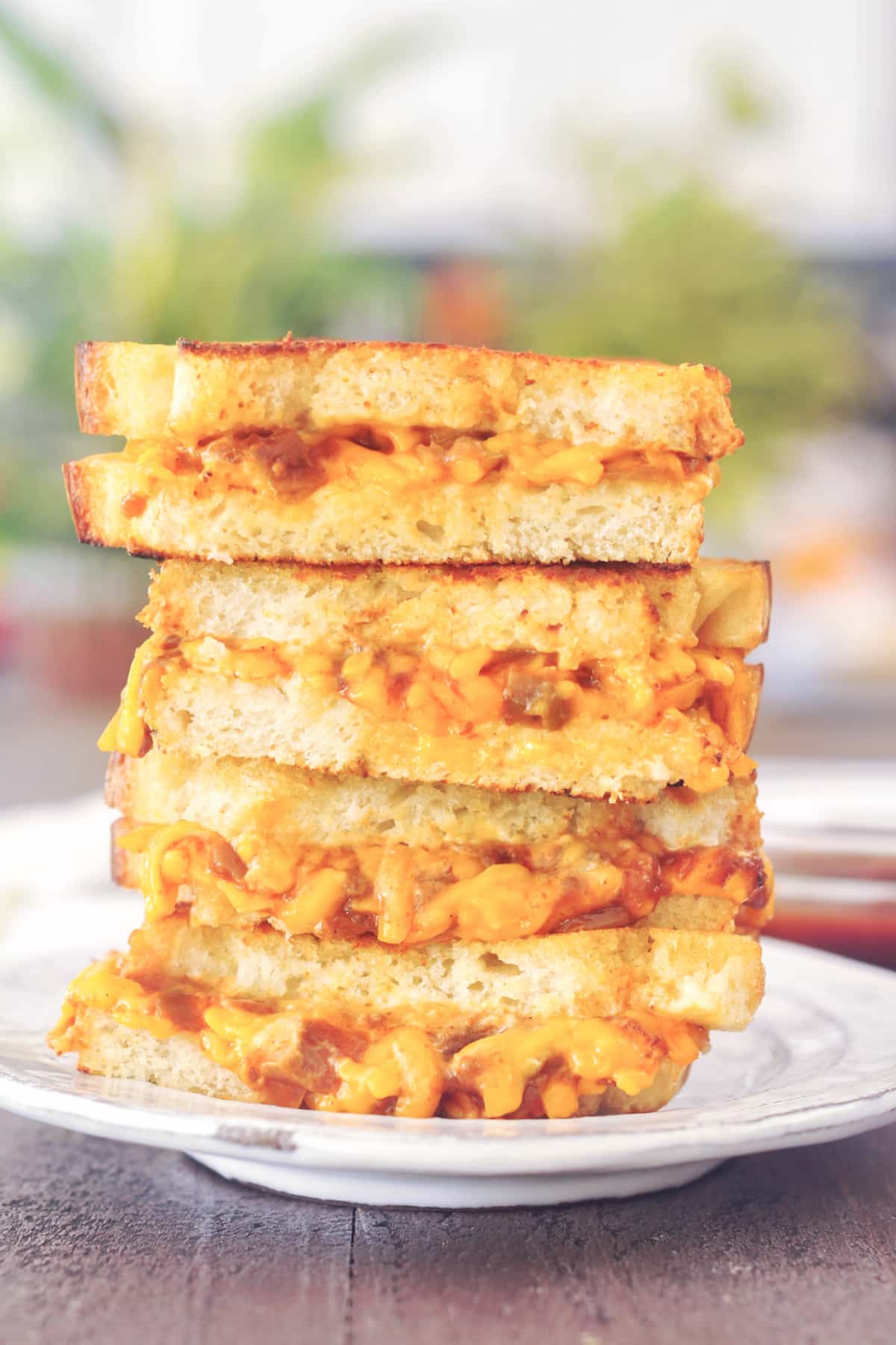 a stack of four sandwich halves of salsa cheddar grilled cheese on a rustic white plate. blurred background of plants.