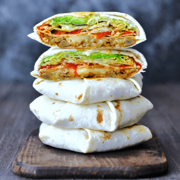 Homemade vegan crunchwrap supreme sliced in half to show filling and stacked five layers high (two halves on top of three whole crunchwraps). filling is beans, cheese, crunchy tortilla, red peppers, salsa, iceberg lettuce.