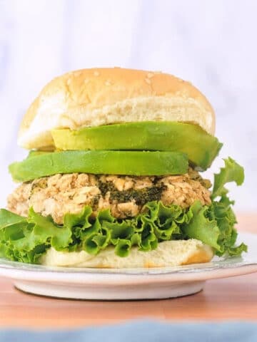 a single white bean veggie burger on a rustic white plate, dressed with curly lettuce, avocado, and a soft sesame bun