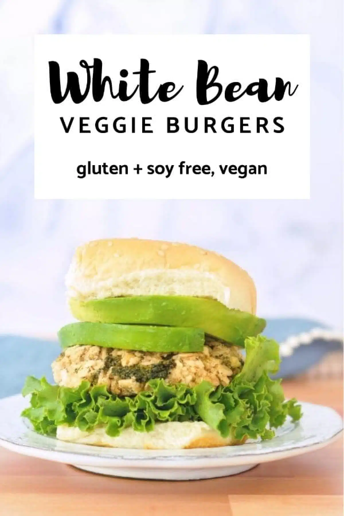 a single white bean veggie burger on a rustic white plate, dressed with curly lettuce, avocado, and a soft sesame bun