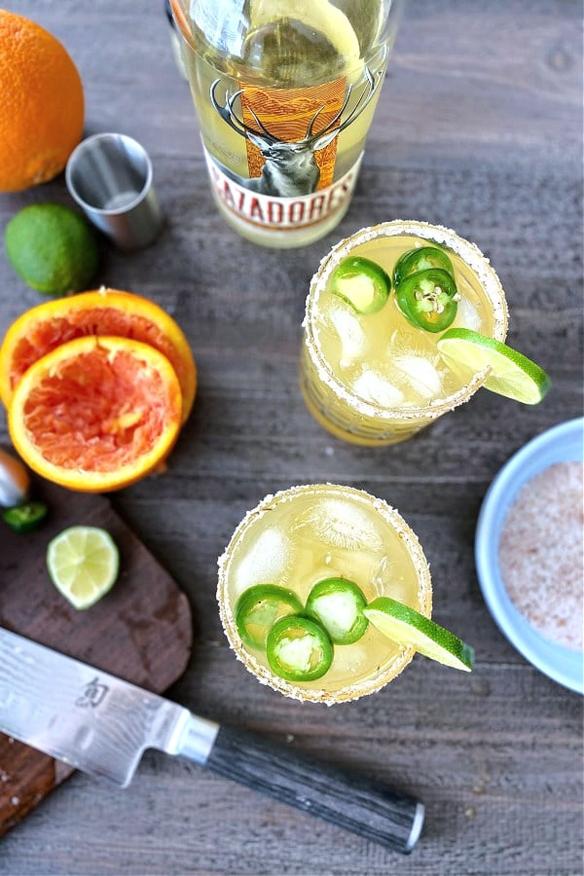 overhead view of jalapeno margaritas, with juiced orange rinds and sliced lime on the side.