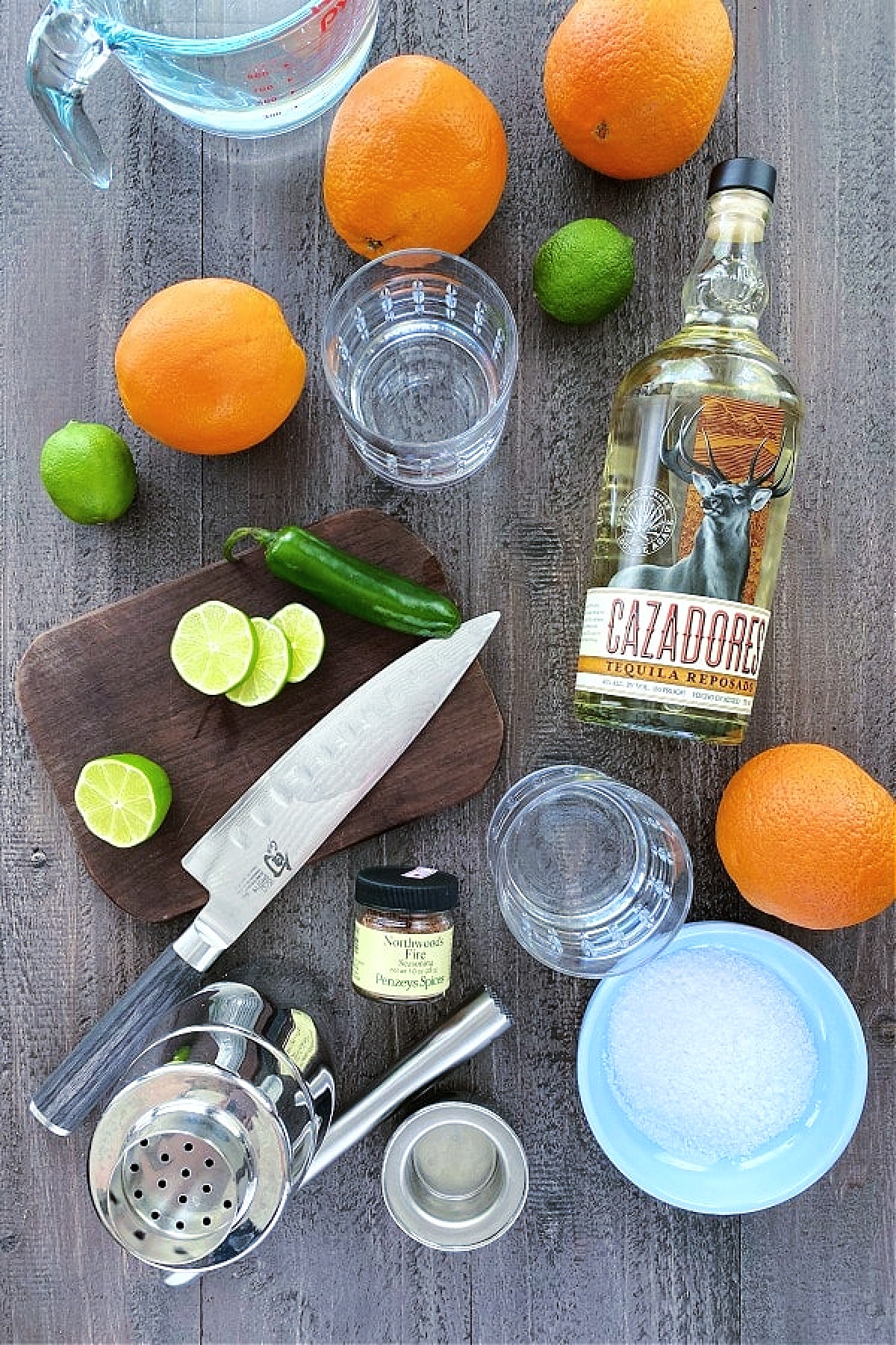 ingredients for making a margarita: fresh oranges, limes, and jalapeno, tequila, salt, soda