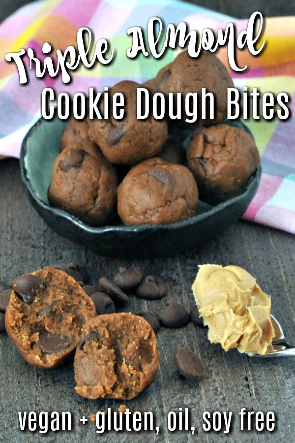 Almond cookie dough bites in bowl, single bite sliced open outside bowl, with spoonful of almond butter and chocolate chips scattered about