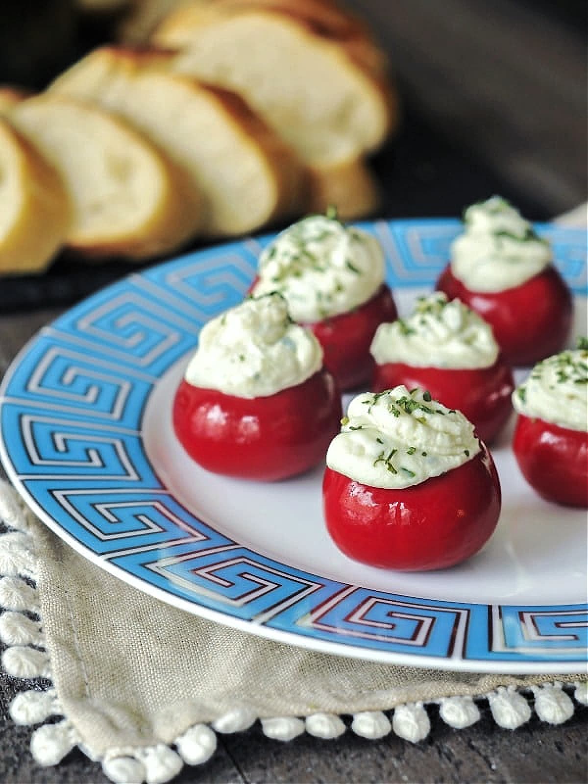 Round red peppadew sweet peppers filled with herb cheese (Boursin style) on a white plate with a light blue Greek Key border design