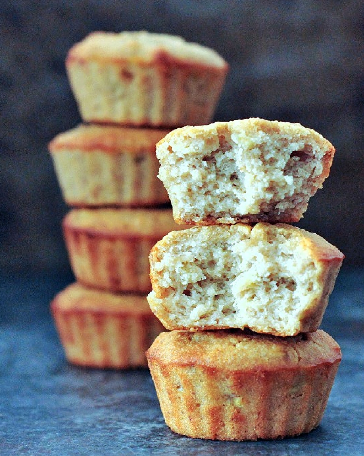 Two stacks of peanut butter banana muffins, with the front stack in focus and one muffin cut in half to show crumb inside.