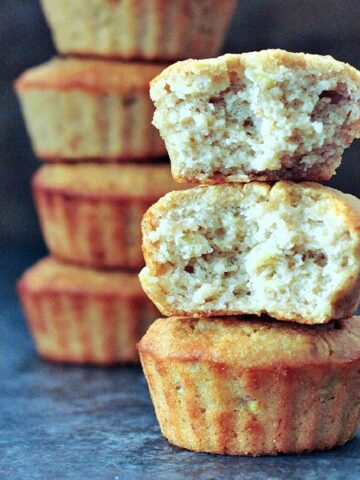Two stacks of peanut butter banana muffins, with the front stack in focus and one muffin cut in half to show crumb inside.